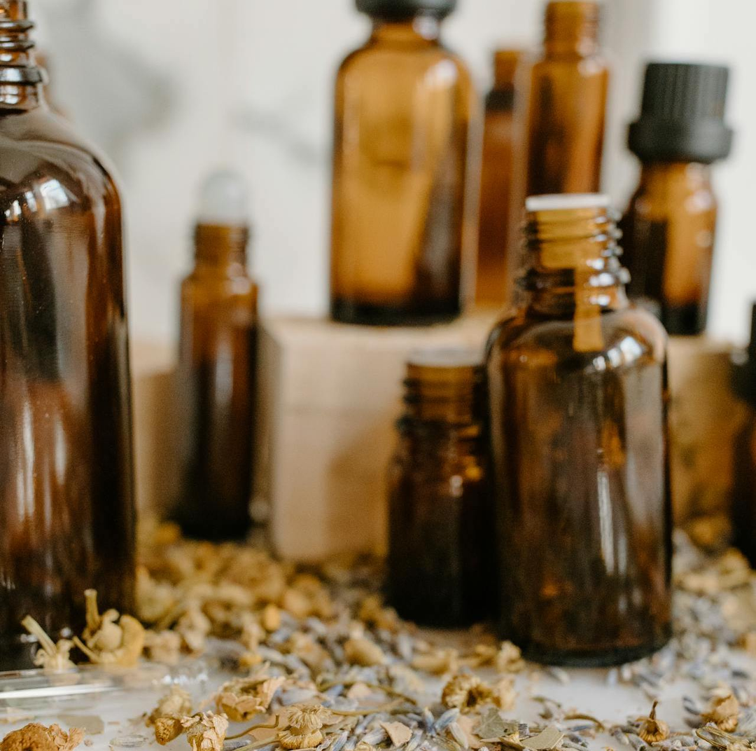 amber bottle and droppers used to package homemade skincare and essiential oil blends on a table with dried flower petals