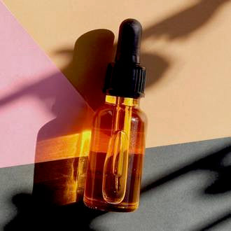 Liquid gold skin replenishing serum from go native nz in a clear glass dropper bottle, on beige, pink and black paper with dappled sunlight